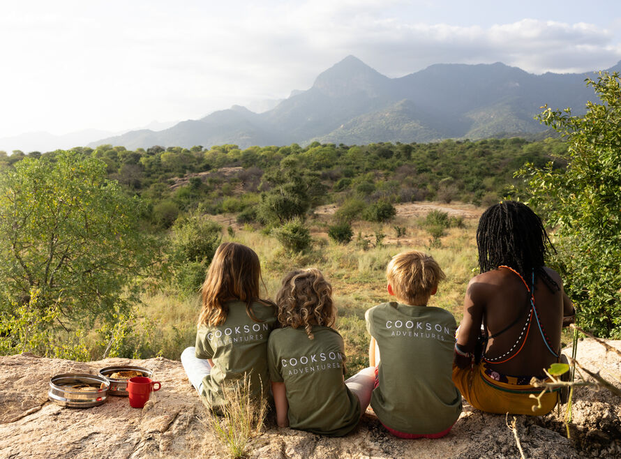 Children sitting with a Samburu warrior at a viewpoint looking out onto a National Park.