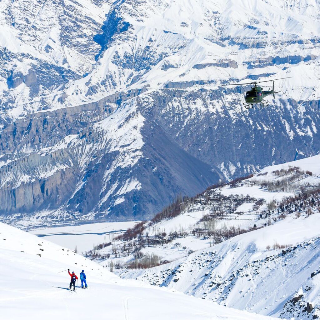 Two skiers wave at their approaching helicopter