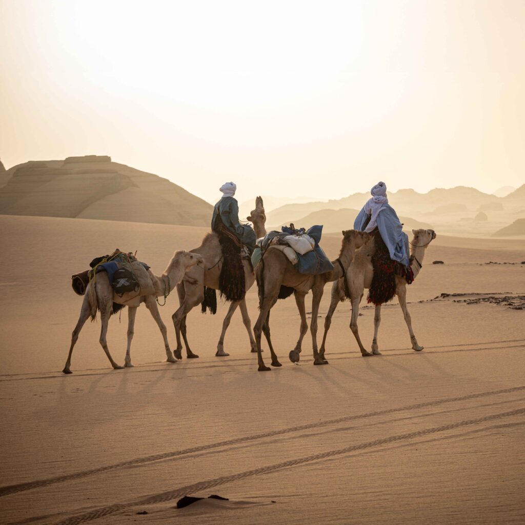 Local people riding camels across the desert.