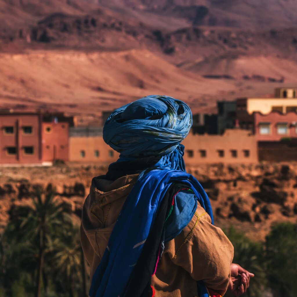 Tuareg person in a blue litham looking out onto a village.